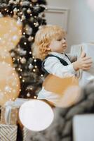 Merry Christmas and Happy Holidays. Cheerful little boy near the Christmas tree with Christmas presents. Children are having fun. Loving family with gifts in the room. photo