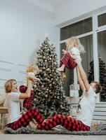 Cheerful and happy family with Christmas gifts near the Christmas tree in matching pajamas. Children are having fun. Loving family with gifts in the room. photo