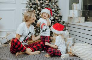 Cheerful and happy family with Christmas gifts near the Christmas tree in matching pajamas. Children are having fun. Loving family with gifts in the room. photo