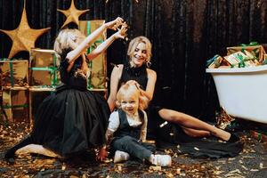 Merry Christmas and Happy Holidays. Cheerful and happy family with christmas gifts in golden packaging and dark background playing with confetti. Loving family with gifts in the room. photo