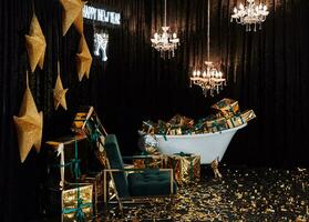 Bathtub with New Year's gifts in gold wrappers on a dark background, green modern armchair with gold armrests, chandeliers hanging from the ceiling photo