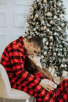 joven hermosa Pareja en pareo rojo pijama cerca el Navidad árbol. alegría, abrazos y besos. nuevo años Días festivos y regalos debajo el Navidad árbol foto