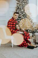 Young beautiful couple in matching red pajamas near the Christmas tree. Joy, hugs and kisses. New Year's holidays and gifts under the Christmas tree photo