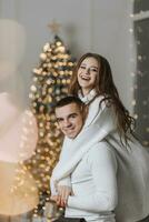 un hermosa y elegante joven familia en blanco suéteres abrazo y alegrarse en el Navidad luces en contra el antecedentes de el Navidad árbol. nuevo año concepto foto