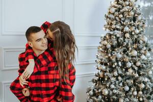 a beautiful young girl in red pajamas stands on the windowsill and puts on a Christmas tree. Christmas concept. Many gifts in paper wrappers under the Christmas tree photo