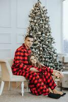 Young beautiful couple in matching red pajamas near the Christmas tree. Joy, hugs and kisses. New Year's holidays and gifts under the Christmas tree photo