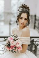 A young girl with a beautiful hairstyle and makeup in a luxurious wedding dress with a bouquet of roses in her hands photo