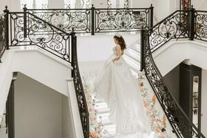 A beautiful woman in a white dress with a long train climbs the stairs in a classic interior. photo