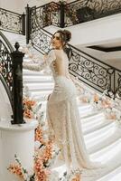 a girl in a luxurious wedding dress with open shoulders on the stairs decorated with flowers. Horizontal photo