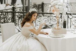 studio photo of a girl in a wedding dress with a luxurious hairstyle and makeup, the bride is sitting at the table