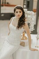 studio photo of a girl in a wedding dress, posing near a table with flowers