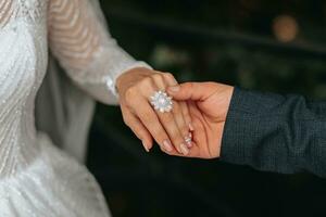 detalles Boda accesorios. el novio sostiene el de la novia mano, un cristal Boda anillo en su mano. recortado foto. hermosa manos foto