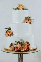 White three-tiered wedding cake decorated with orange roses. Festive dessert table with sweets. Wedding candy bar, various cakes, chocolate on stands. photo