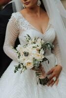 Wedding portrait. A brunette bride in a long dress holds her bouquet of roses, peonies and greenery. Cropped photo. Open bust photo