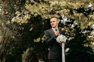 Photo of the groom in a classic black suit with a bouquet of flowers in his hands