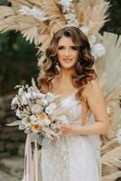 retrato de el novia. el novia soportes en contra el antecedentes de un arco hecho de flores y seco flores elegante Boda vestido. Boda decoraciones rural estilo foto