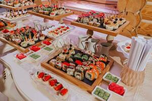 Big buffet reception of different delicious food at a wedding celebration. Snacks for guests. Wedding party. Canapes, sushi, fruit, meat, drink, wine, juice. photo