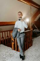 A young businessman in a hotel room is dressed in a classic gray suit, a white shirt and a bow tie. Rest in wonderful apartments. Groom's morning at the hotel. Male hands close up photo