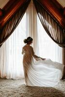 A girl with a beautiful hairstyle against the background of a window in the backlight throws up her robe photo