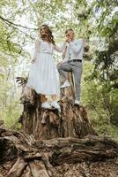 Wedding walk in the forest. The groom holds the bride's hand and they stand on a large tree stump. Vertical photo