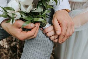 The bride and groom gently hold hands. They hold a bouquet in their hands. Close-up photo