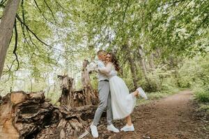 Wedding walk in the forest. The bride and groom rejoice and kiss, tall trees near them. Country wedding concept. Wide angle photo. photo