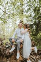 amable abrazo de el novia y novio en el bosque. el novio es vestido en un blanco camisa y gris pantalones, el novia es en un ligero blanco vestir foto