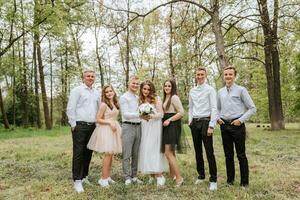 Wedding walk in the forest. Brides and their friends pose against the background of the forest. A large group of people are having fun at their friends' wedding photo