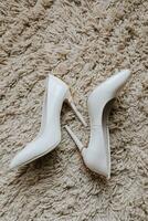 Women's white high-heeled shoes lie on a blanket. Details of the bride photo