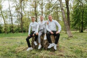 The groom and his friends are posing against the background of the forest. not a large company of people having fun. Smiling boys sit on a stump and rejoice together with the bridegroom photo