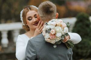 The groom embraces the bride and kisses her, the bride looks at the groom. Wedding walk in the garden photo