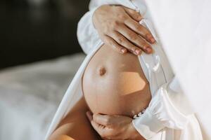 studio portrait, close-up, of a beautiful pregnant young woman on a white bed, holding her pregnant belly with her hands photo