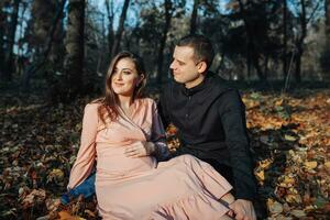 A man touched his pregnant wife's belly with his hand while resting in an autumn forest on a yellowed leaf. Support of the husband during pregnancy photo