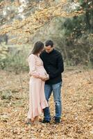 portrait of a happy young family, husband and pregnant wife, standing against the background of beautiful light in the autumn forest, looking at each other photo