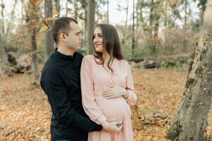 un hombre y su embarazada esposa abrazo en el bosque a atardecer, esperando para el nacimiento de un niño. contento familia concepto. foto