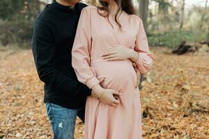 Close-up photo. A man and his pregnant wife embrace in the forest at sunset, waiting for the birth of a child. Happy family concept. photo