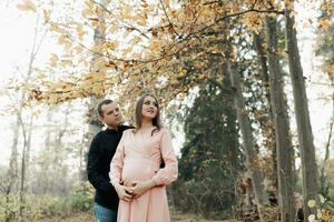 un hombre y su embarazada esposa abrazo en el bosque a atardecer, esperando para el nacimiento de un niño. contento familia concepto. foto