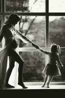 Studio portrait of a beautiful pregnant young woman near the window with her daughter. Black and white photo