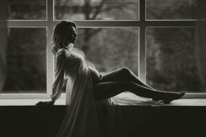 estudio retrato, de cerca, de un hermosa embarazada joven mujer en un blanco cama, participación su embarazada barriga con su manos foto
