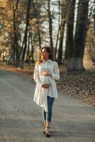 retrato de un contento y hermosa embarazada mujer mirando a el ligero en el parque a puesta de sol. el belleza de un mujer durante el embarazo. cómo a ser contento y sano en otoño. otoño humor. foto