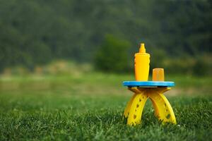 Sunscreen on the background of green mountains. Orange plastic bottle with sun protection on children's chair and green lawn photo