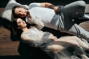 photo of a young pregnant woman in her room in a white lace dress on the floor with her husband in beautiful sunlight. Motherhood. Concept of pregnancy, motherhood, preparation and waiting.