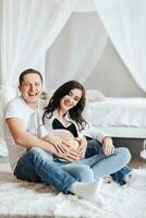 modern beautiful pregnant woman in jeans and shirt with her husband at home, caring, hugging, kissing. Concept of pregnancy, motherhood, preparation and waiting. The beauty of a woman during pregnancy photo