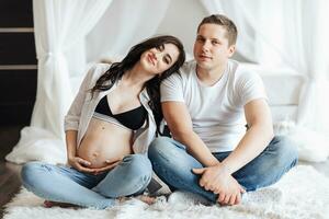 moderno hermosa embarazada mujer en pantalones y camisa con su marido a hogar. concepto de el embarazo, maternidad, preparación y espera. el belleza de un mujer durante el embarazo foto