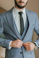 cropped portrait of a stylish man with a black beard in a shirt, jacket and tie, with a strong watch on his hand photo