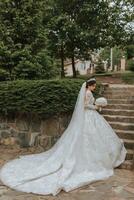 el novia en un hermosa blanco vestir con un largo tren y un ramo de flores de hortensias en su manos foto