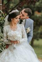 European wedding couple in the park. The bride in a beautiful dress with sleeves and a crown on her head. Groom with a black beard of Caucasian appearance in a classic suit photo