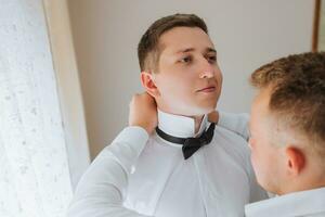 friends help the groom tie his bow tie and prepare for the wedding photo