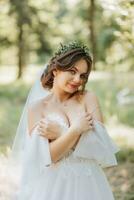 Portrait of a beautiful cute bride girl in an elegant white dress posing on the background of greenery in the forest on a sunny summer day photo