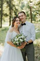 Fashionable groom and cute bride in white dress with tiara of fresh flowers, hugging, laughing in park, garden, forest outdoors. Wedding photography, portrait of smiling newlyweds. photo